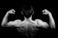 Black and white photo of a muscular man flexing arms against a dark background.