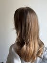 Back view of a woman with long, straight brown hair against a white background.