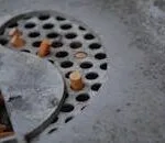 Detailed view of cigarette butts in a metal ashtray with perforated design, depicting usage and waste.