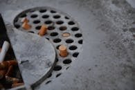 Detailed view of cigarette butts in a metal ashtray with perforated design, depicting usage and waste.