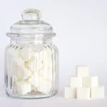 A clear glass jar filled with sugar cubes next to stacked cubes on a white background.