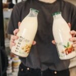 Person holding bottles of almond and soy milk substitutes in a store.