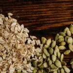 A detailed view of oats and pumpkin seeds arranged on a rustic wooden table.