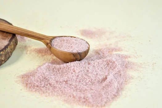 Pink Himalayan salt scattered with a wooden spoon on a light background.