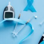 Flat lay of a glucose meter, syringe, and blue ribbon symbolizing diabetes awareness.